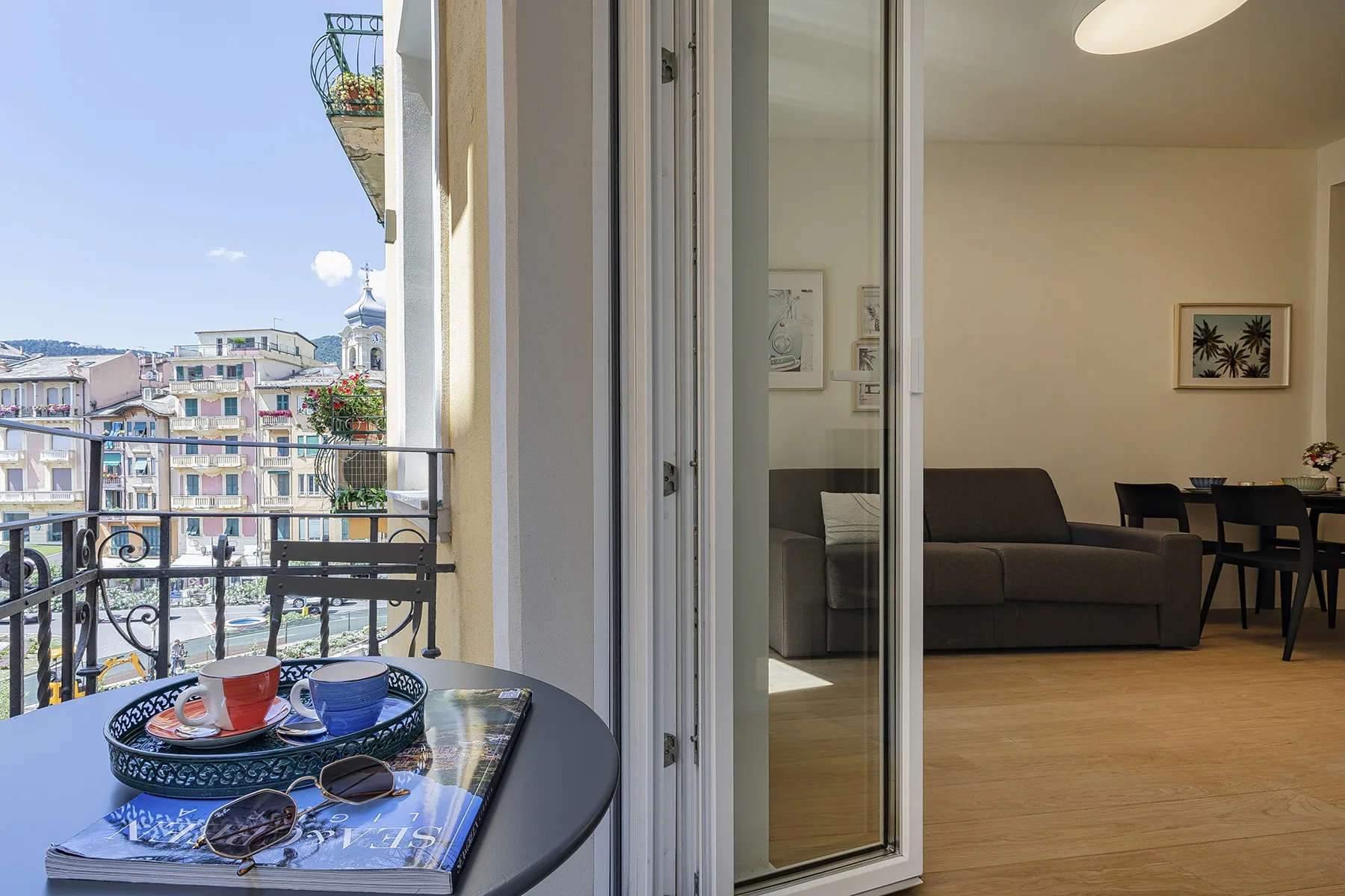 A balcony seating area overlooks nearby buildings, with an adjoining living and dining space.