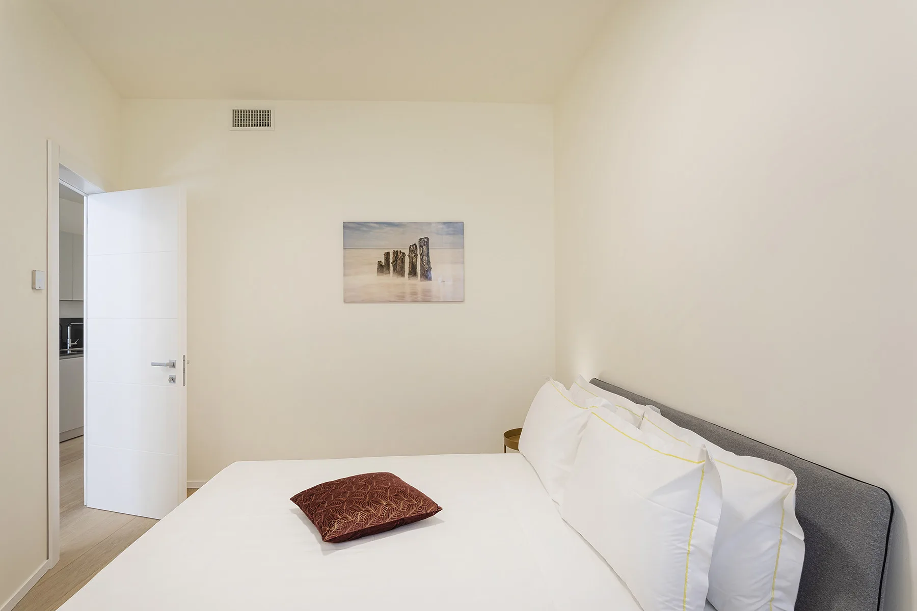 A bedroom with a bed, white pillows, and a small wall picture.