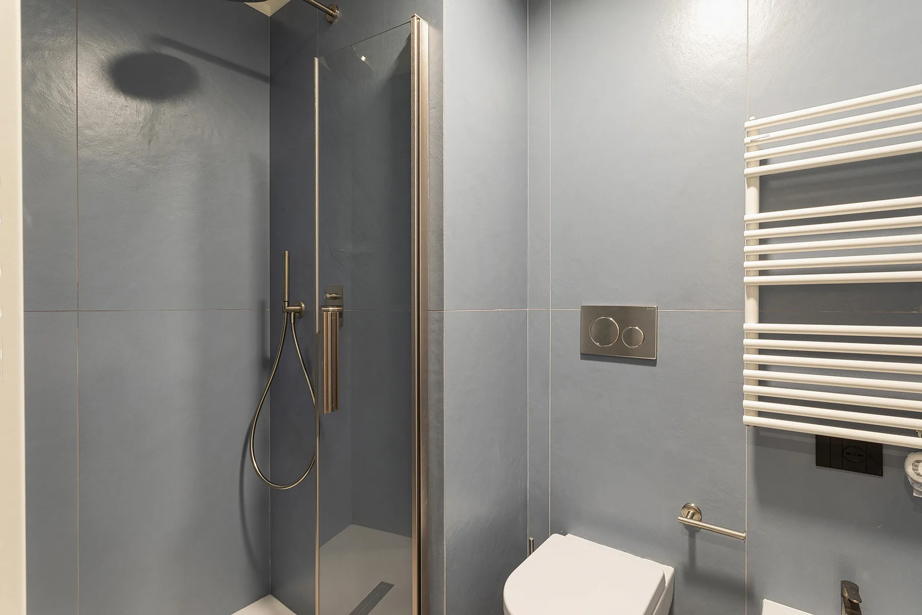 A tiled bathroom with a glass shower, toilet, and wall-mounted towel warmer.