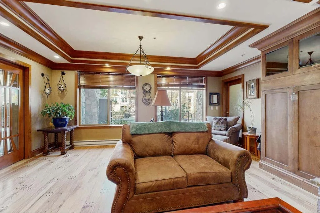 Una sala de estar con un sofá marrón y ventanas grandes.