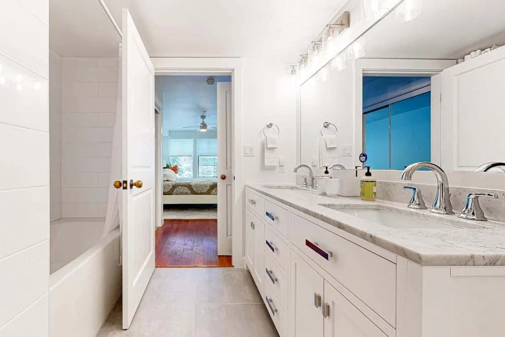 Un baño luminoso con un tocador largo y una puerta abierta a un dormitorio.