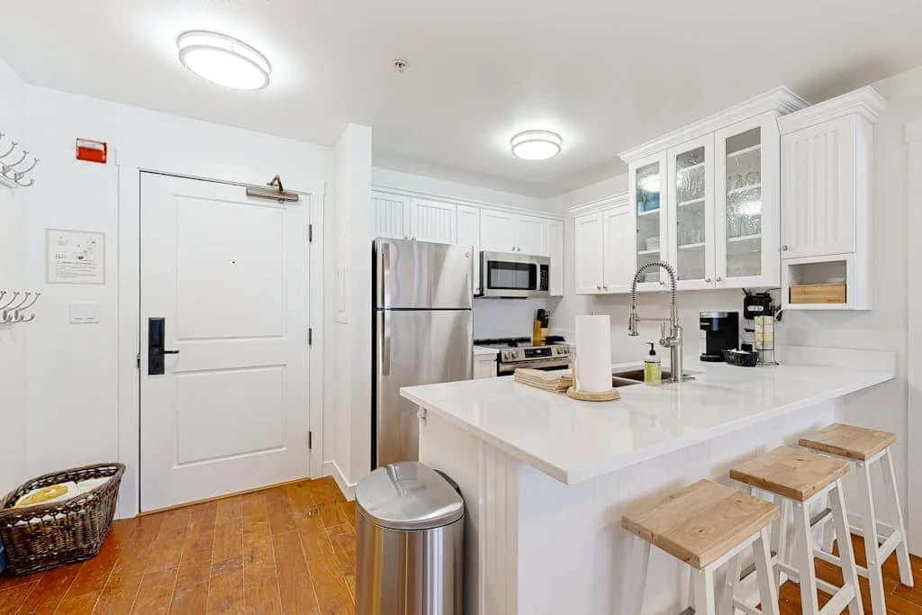 Una cocina blanca y luminosa con una isla grande y electrodomésticos de acero inoxidable.