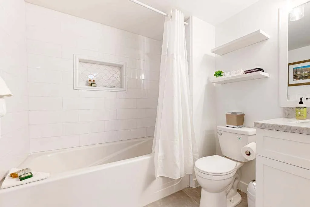 Un baño luminoso con azulejos, bañera, cortina de ducha, inodoro y lavabo.