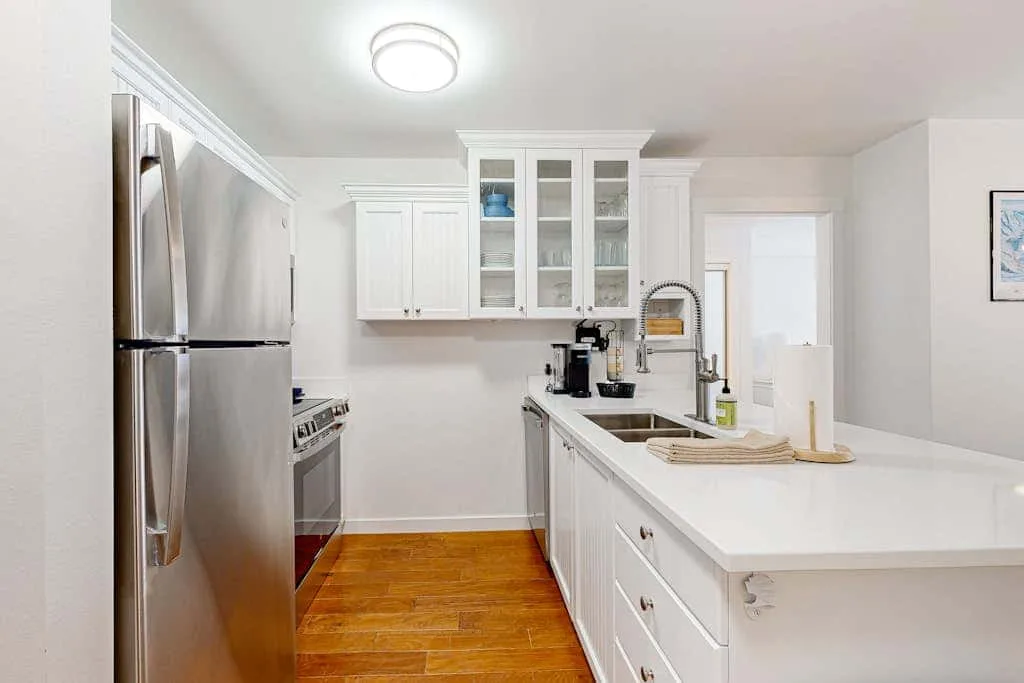 Una cocina blanca y luminosa con electrodomésticos de acero inoxidable y una isla larga.