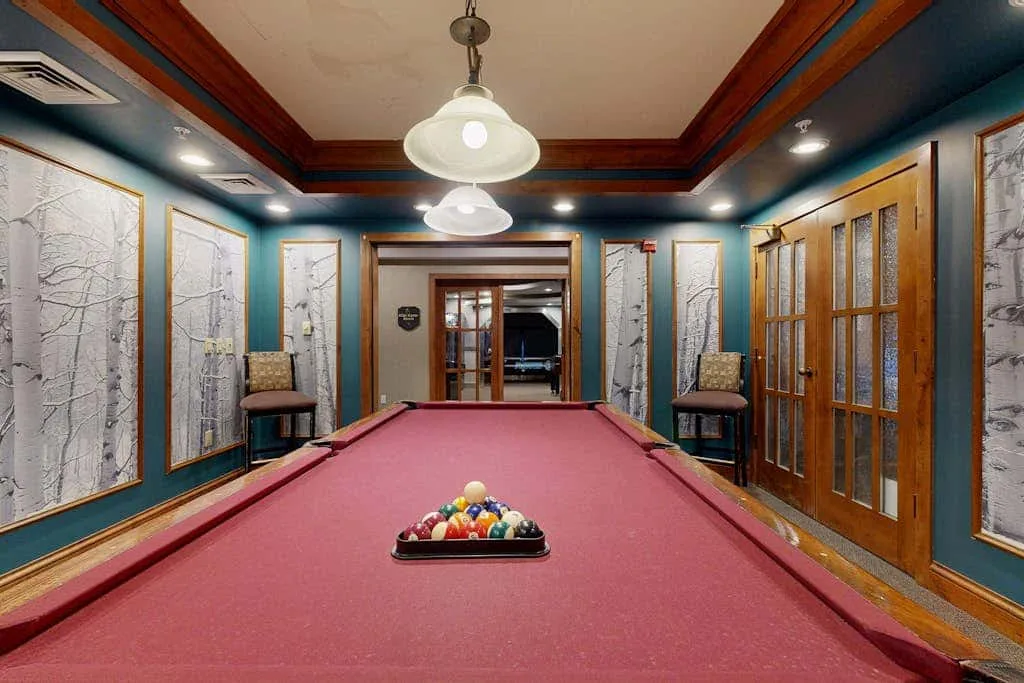 Una sala de billar con una mesa de paño rojo y cuadros en las paredes.