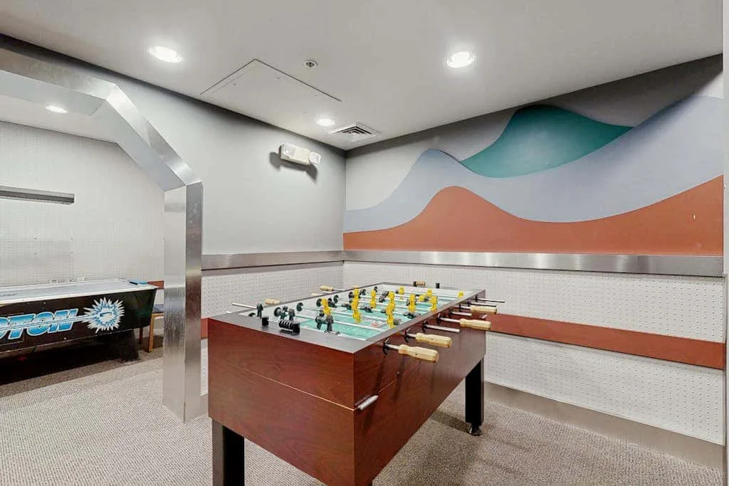 Una sala de juegos con una mesa de futbolín bajo murales de ondas coloridas.