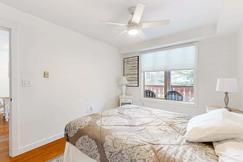 Un dormitorio luminoso con una cama bajo una ventana y un ventilador de techo.