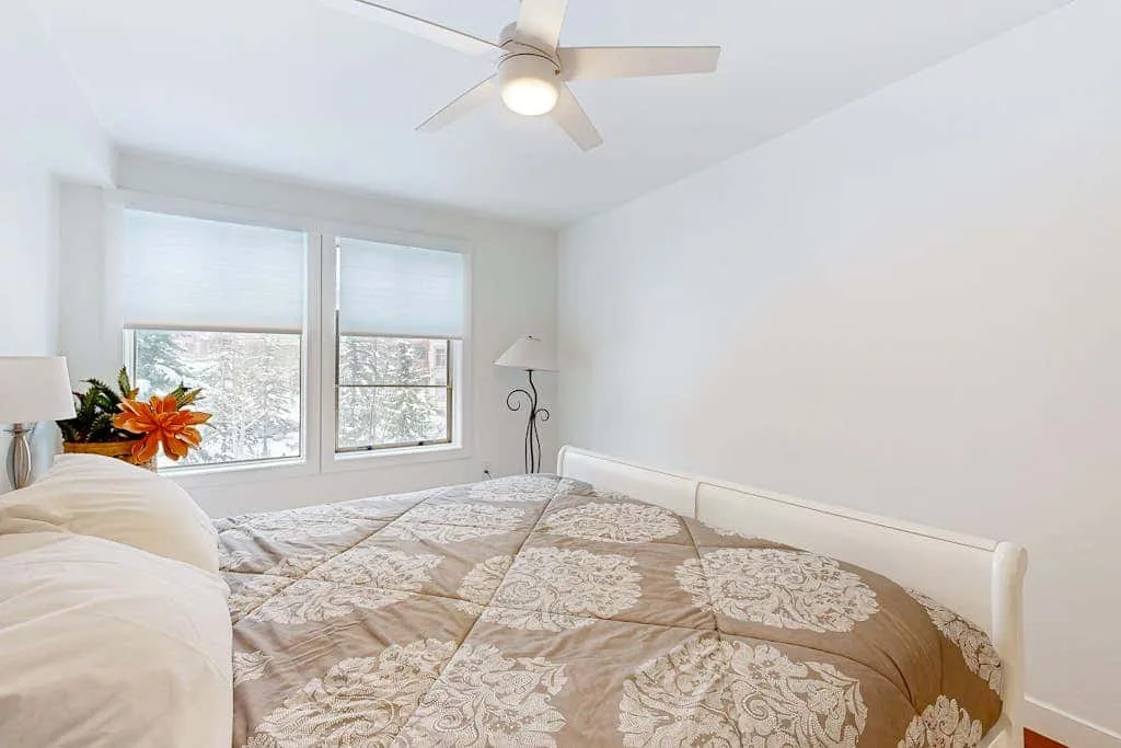 Un dormitorio luminoso con una colcha estampada y dos ventanas.