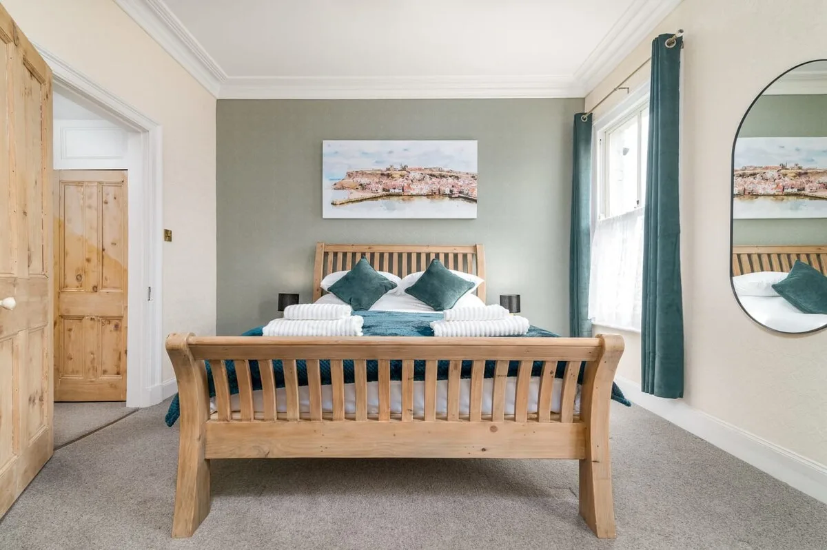 A bedroom with a wooden bed, teal cushions, and a framed picture above it.
