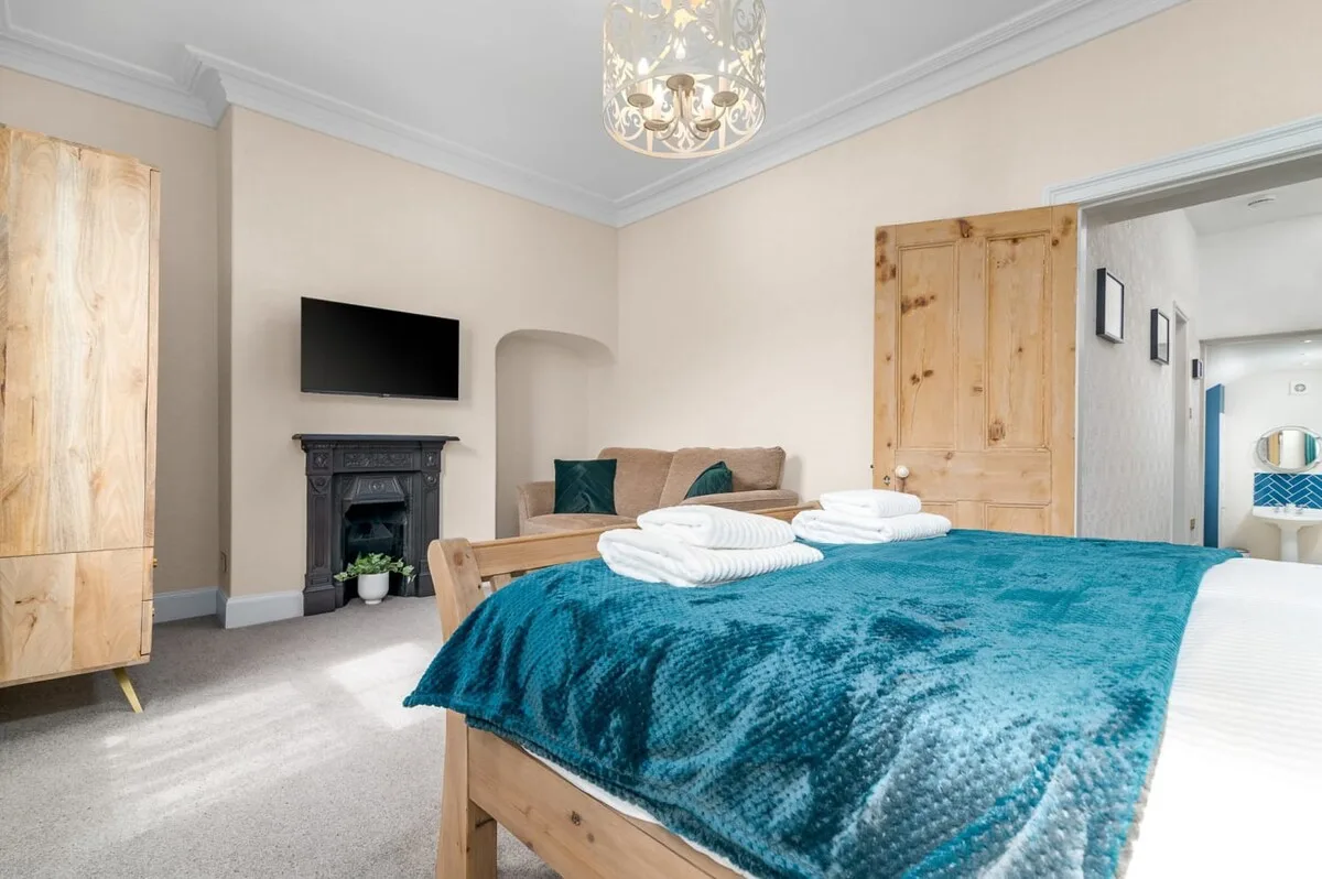 A bedroom with a bed covered in teal bedding and a television above the fireplace.