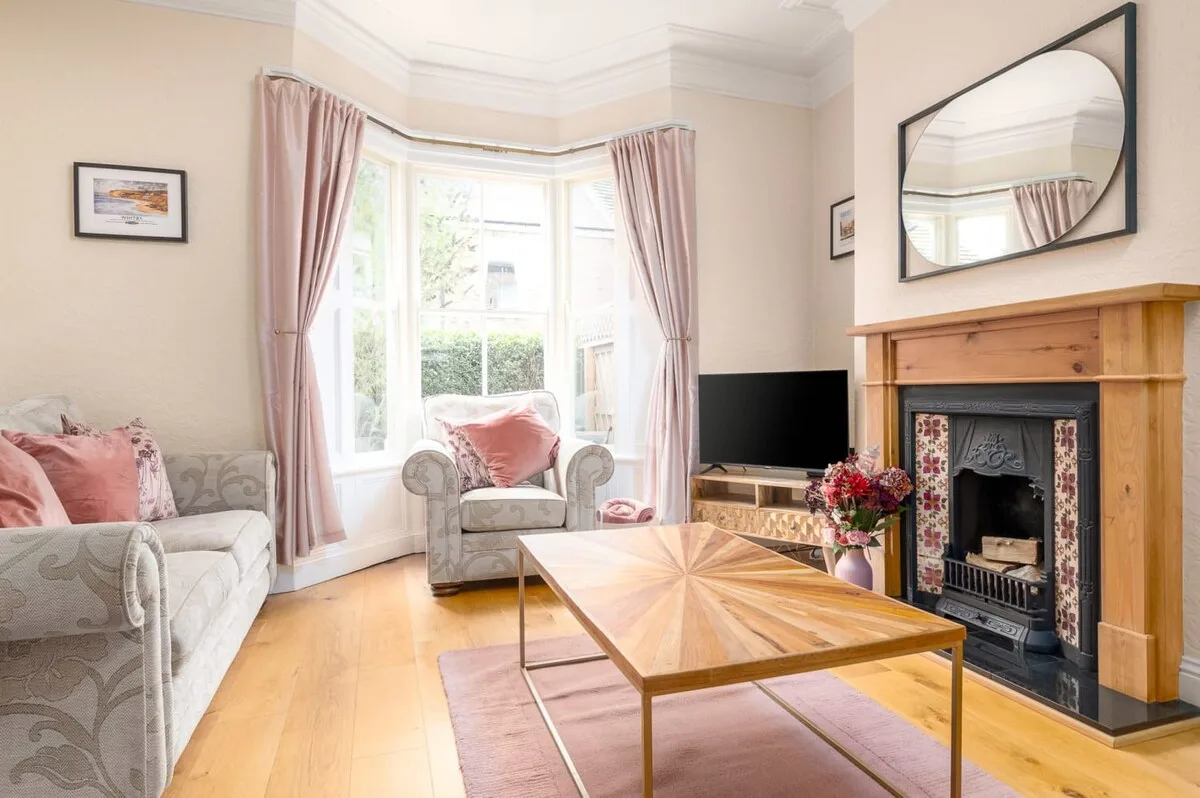 A bright living room with seating, a television, and a wooden fireplace surround.
