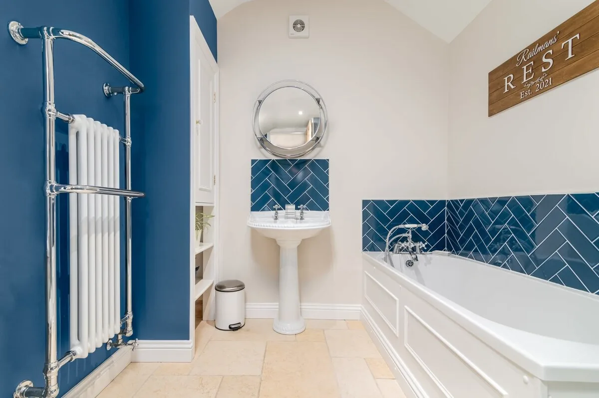 A bright bathroom with a bathtub, pedestal sink, and blue tiled walls.