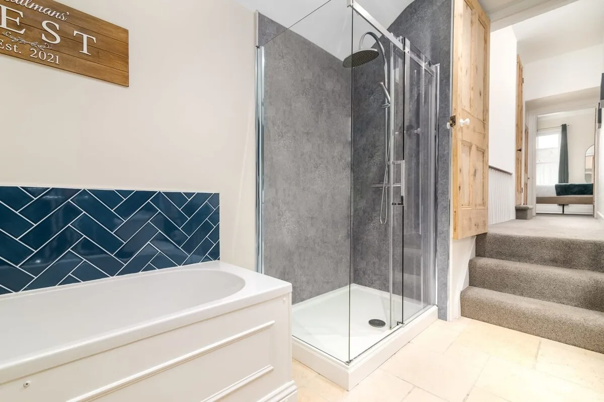 Bathroom with a bathtub, glass shower, and blue tile backsplash.