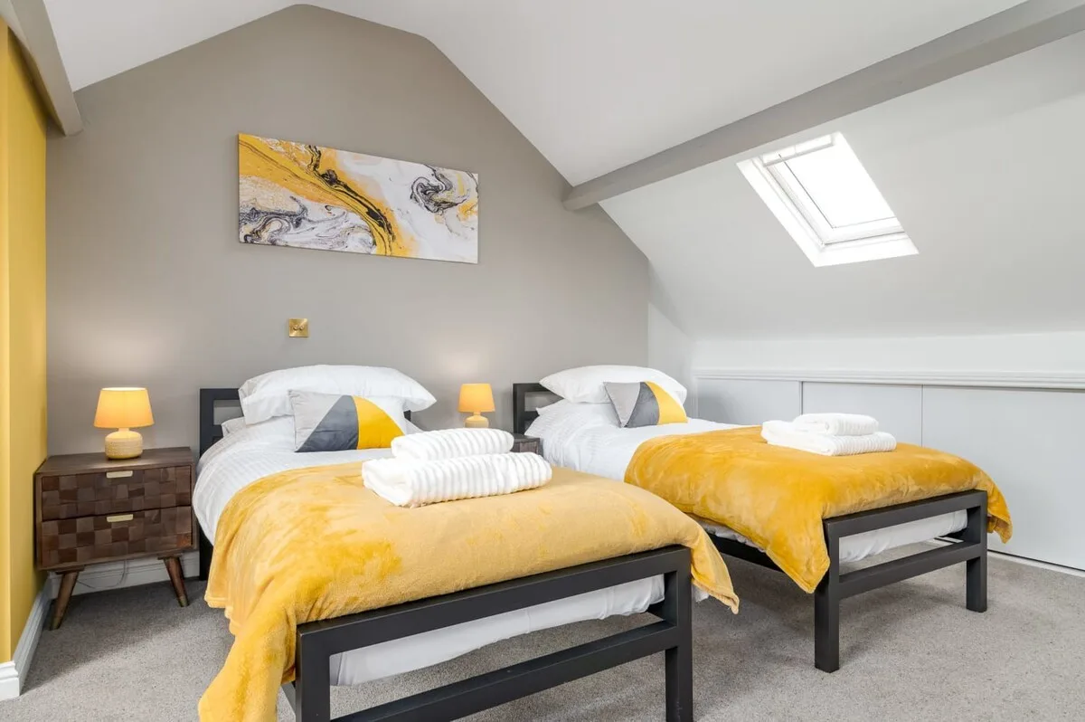 A bright bedroom with two beds dressed in yellow blankets beneath a skylight.