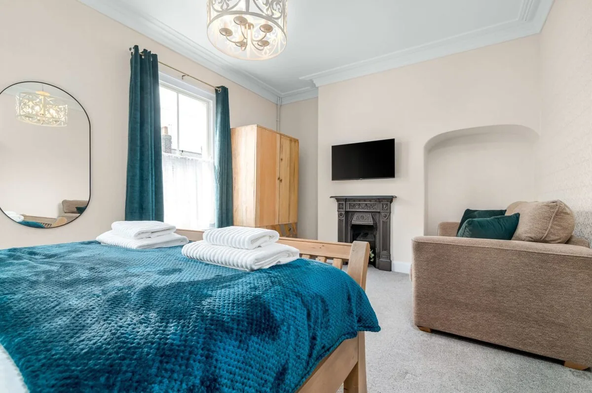 A bedroom with a teal-covered bed, television, and seating area.