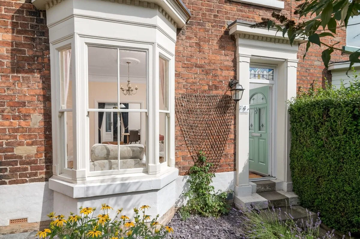 A brick house exterior with a white bay window and green front door.