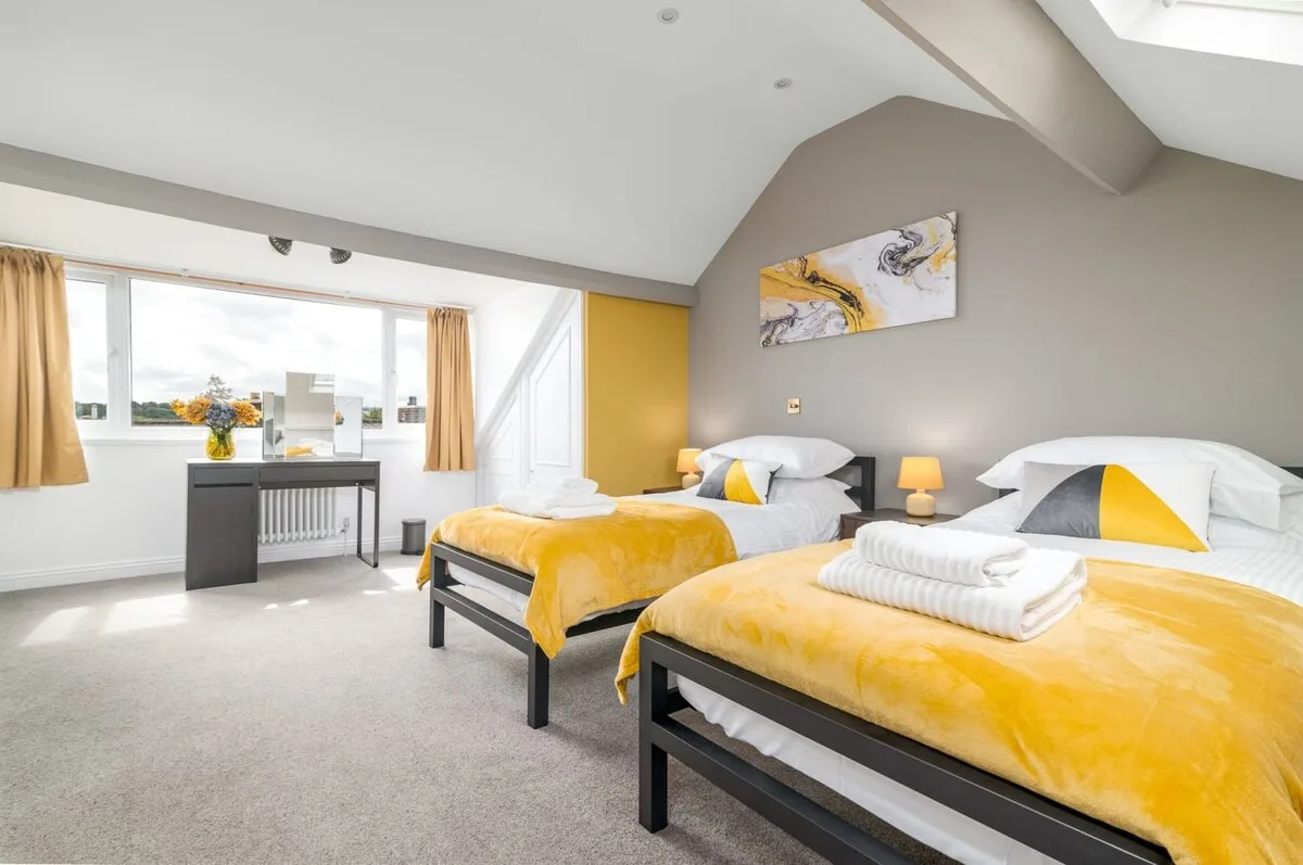 A bright bedroom with two beds dressed in yellow covers.