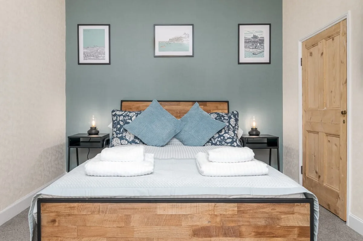 A bedroom with a neatly made bed and framed prints above the headboard.