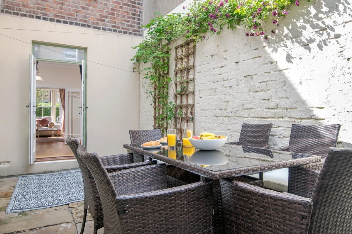 An outdoor patio dining area with a table and seating beneath flowering vines.