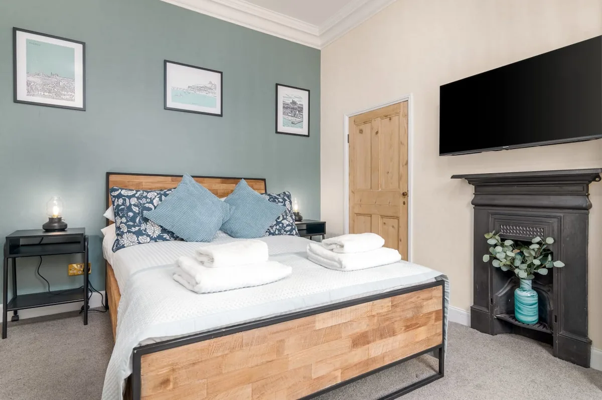A bedroom with a wooden bed, white bedding, and a wall-mounted television.