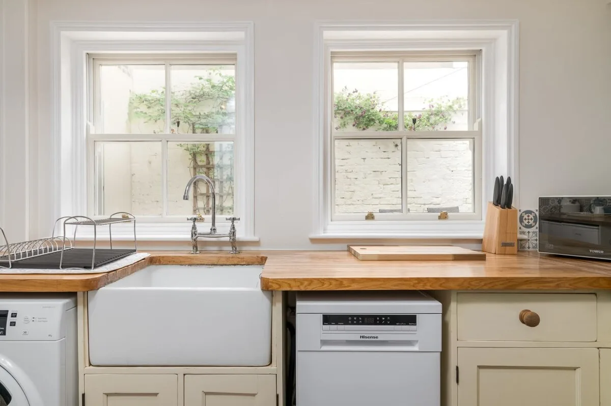 A bright kitchen with a sink beneath two windows and a dishwasher.