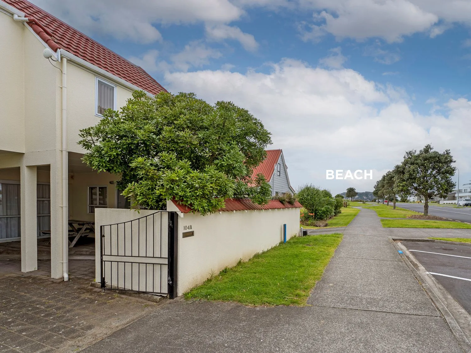 Una casa con portón de entrada y techo de tejas junto a una acera con árboles en Sans Souchi - Whangamata Holiday Home, en Whangamata