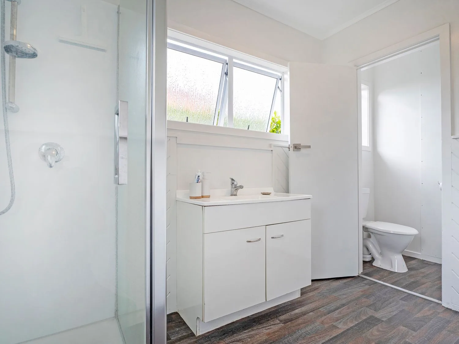 Un baño con una ducha de cristal, un mueble de lavabo blanco y un aseo separado.