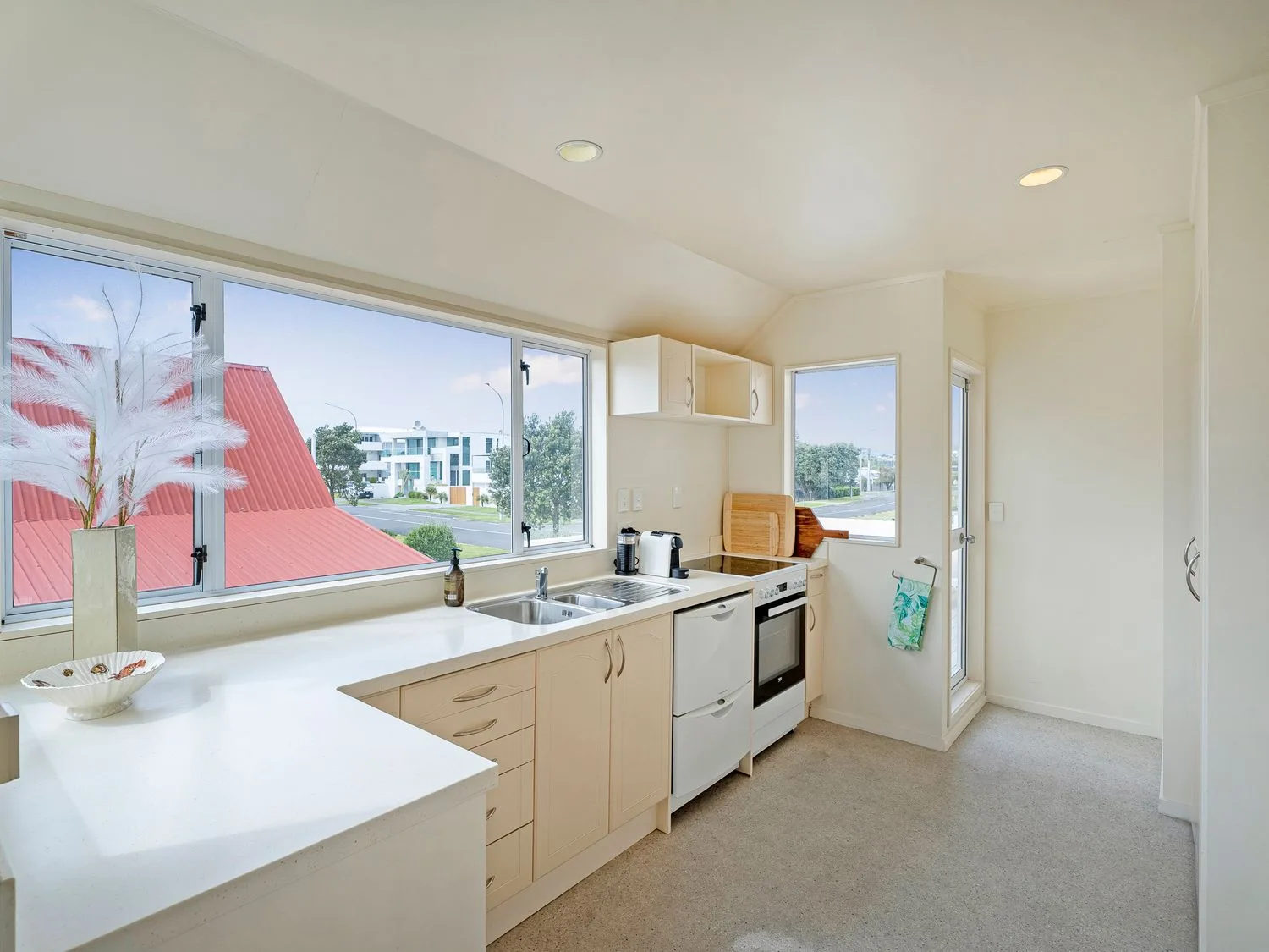 Una cocina con armarios, fregadero, cocina, lavavajillas, tablas de cortar y grandes ventanas en Sans Souchi - Whangamata Holiday Home, en Whangamata