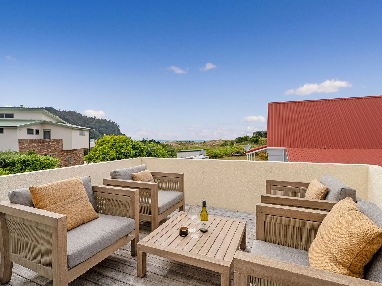 An outdoor seating area with cushioned chairs around a wooden table overlooks nearby homes and greenery.