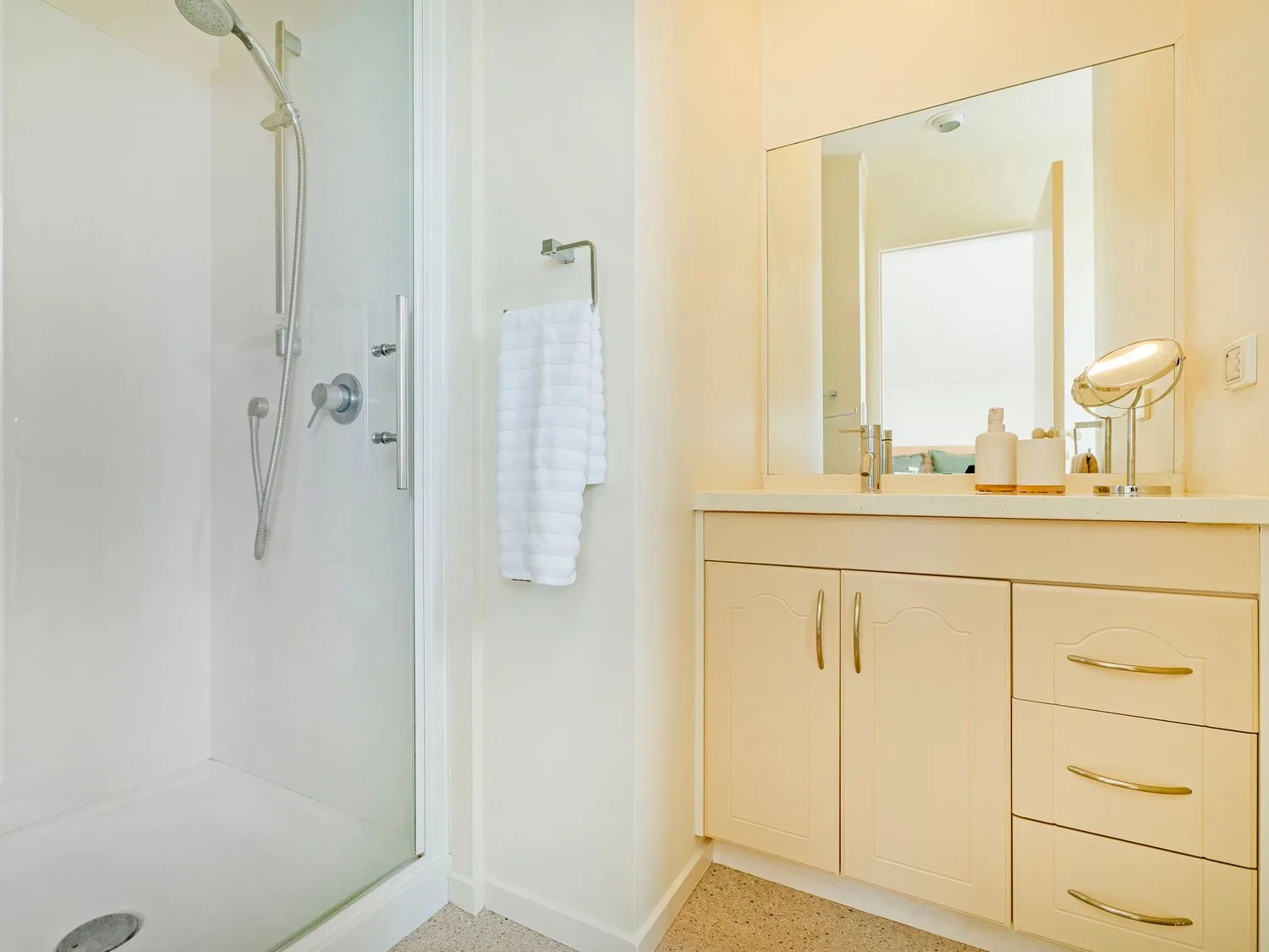 Un baño con una ducha con mampara de cristal, una toalla blanca en un toallero y un mueble de lavabo con un espejo grande en Sans Souchi - Whangamata Holiday Home, en Whangamata