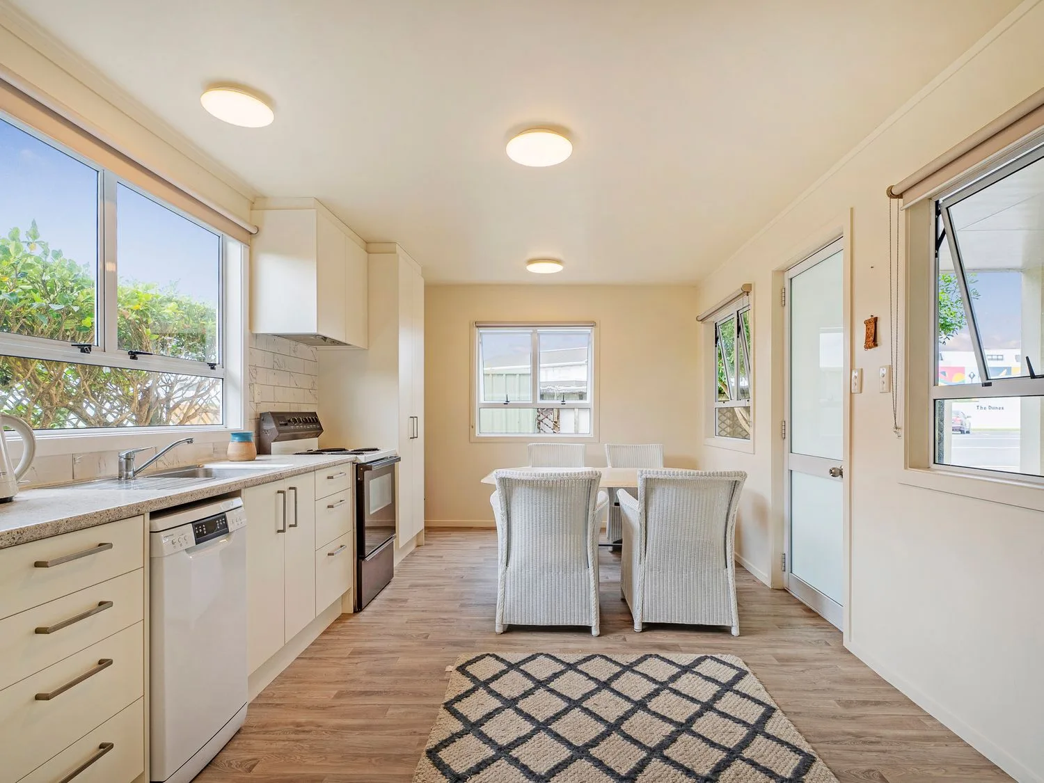 Una cocina y comedor luminosos con una mesa, asientos y ventanas grandes.