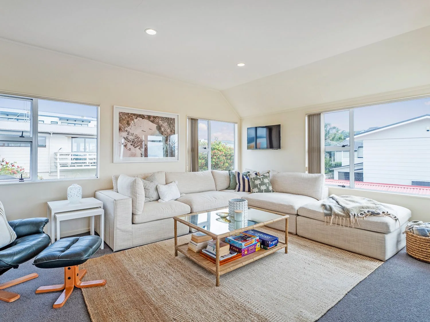 A living room with a large sectional sofa a glass coffee table and a black leather chair with ottoman at Sans Souchi - Whangamata Holiday Home in Whangamata