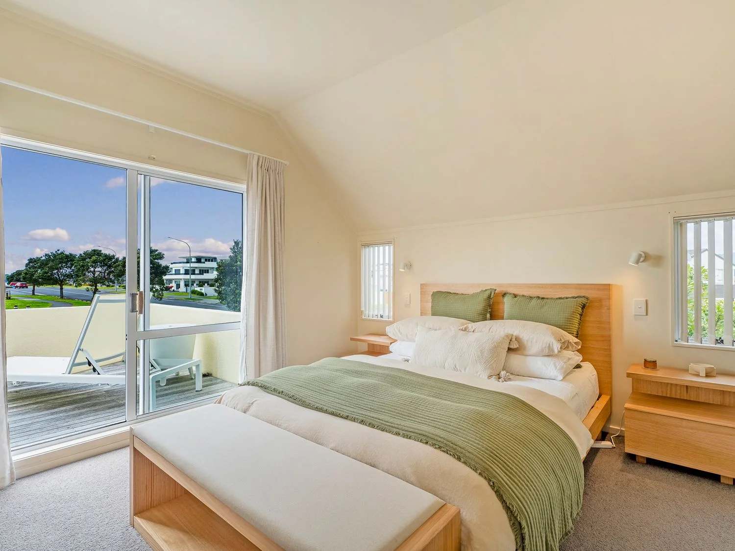 Un dormitorio con una cama, un banco a los pies de la cama y puertas correderas que dan a un balcón en Sans Souchi - Whangamata Holiday Home, en Whangamata