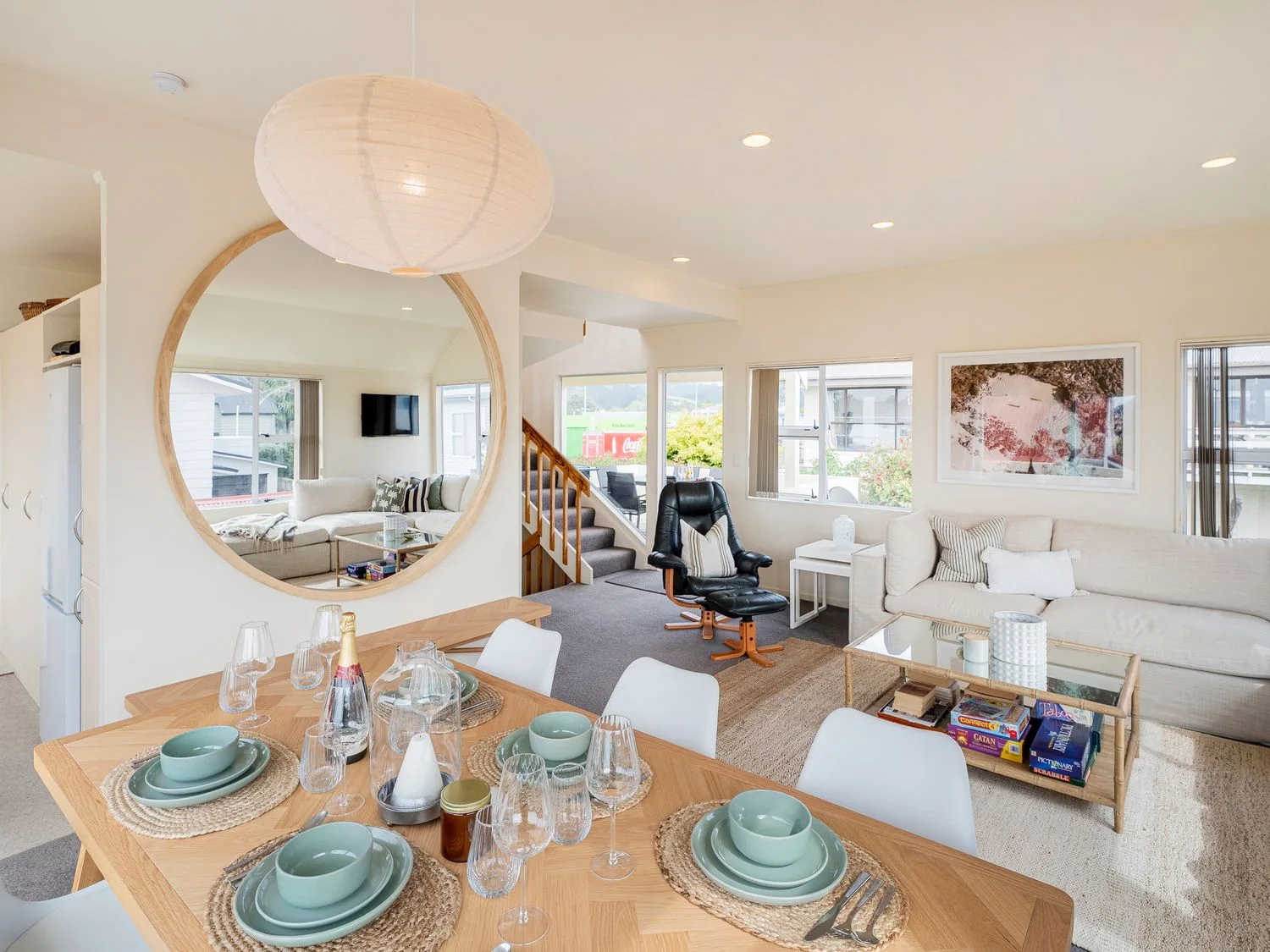 Un comedor con la mesa puesta y una sala de estar con un sofá y un sillón en Sans Souchi - Whangamata Holiday Home, en Whangamata