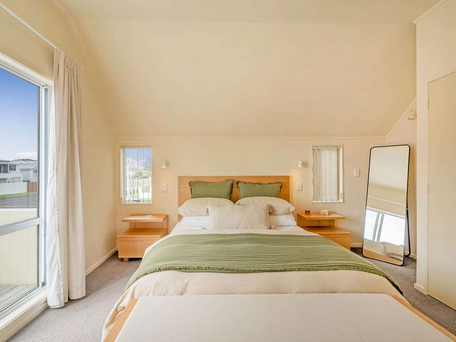 Un dormitorio con una cama con una manta verde, dos mesitas de noche de madera y un espejo de pie en Sans Souchi - Whangamata Holiday Home, en Whangamata