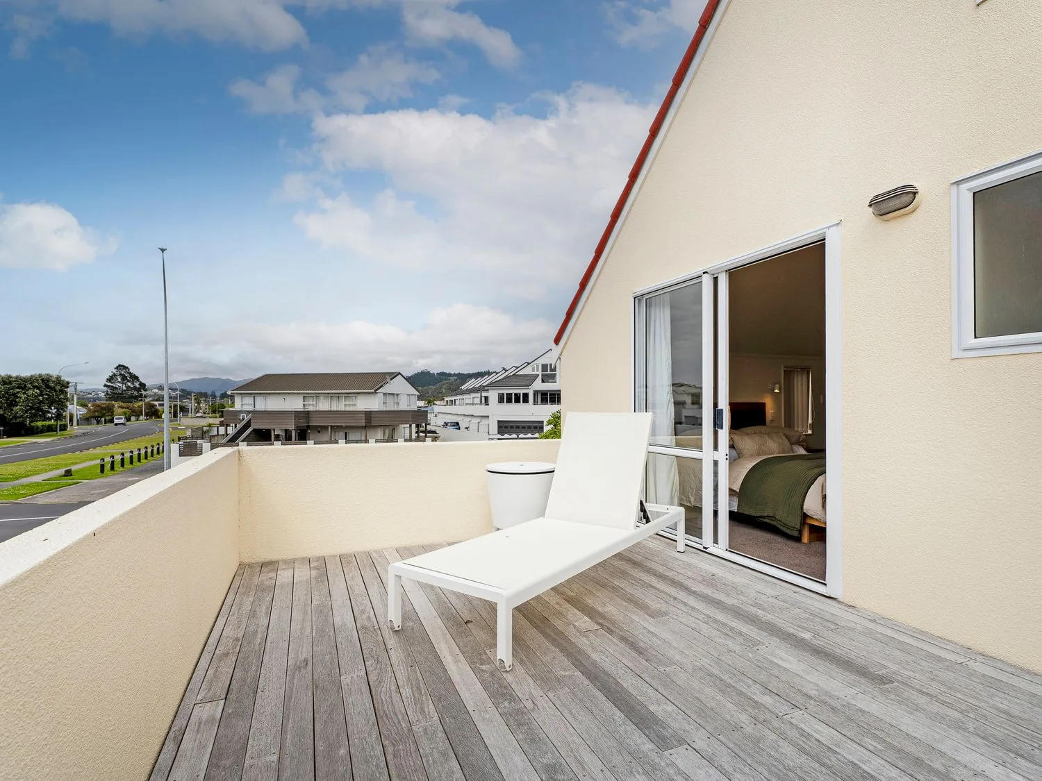 Un balcón con una tumbona blanca y una puerta corredera de cristal que da a un dormitorio en Sans Souchi - Whangamata Holiday Home, en Whangamata