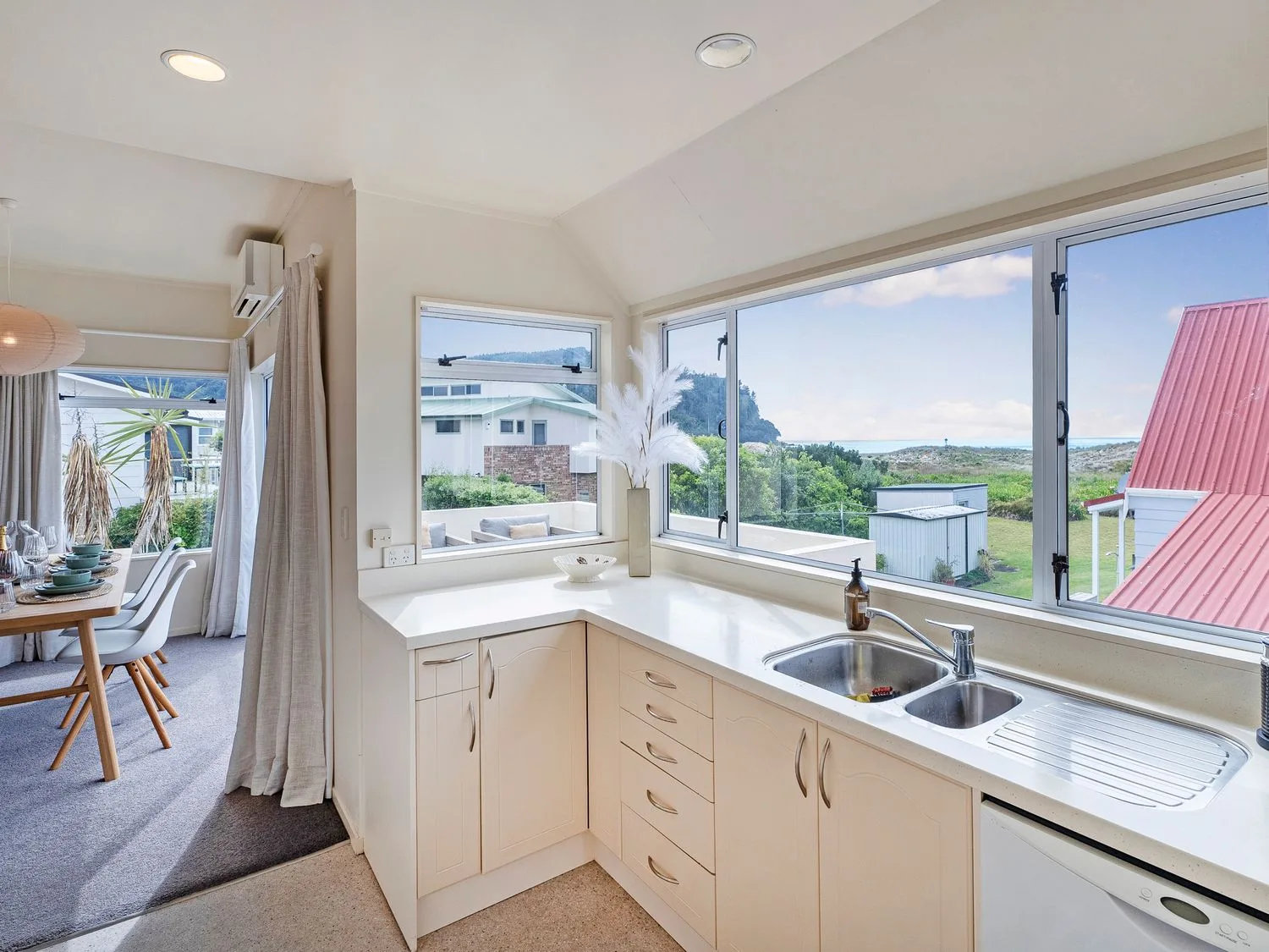 Una cocina con un fregadero doble y una encimera junto a ventanas con vistas al exterior en Sans Souchi - Whangamata Holiday Home, en Whangamata