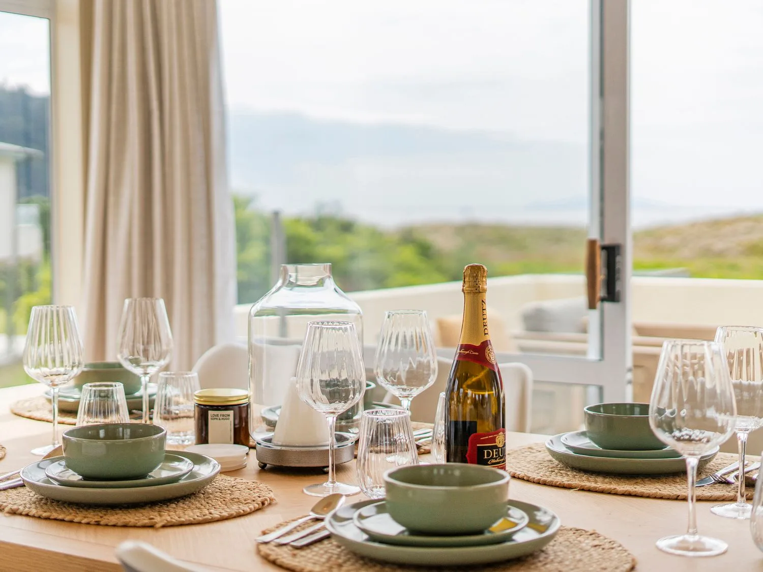 Una mesa de comedor puesta con cuencos, platos, copas de vino y una botella en Sans Souchi - Whangamata Holiday Home, en Whangamata
