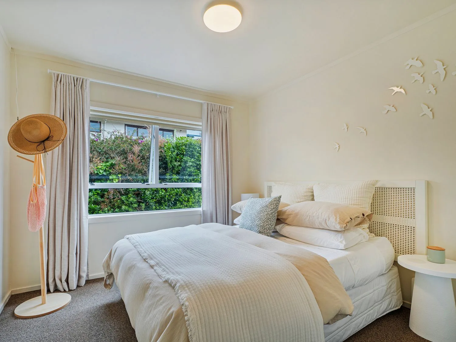 Un dormitorio con una cama, almohadas, una mesita de noche, un perchero de pie y una ventana con cortinas en Sans Souchi - Whangamata Holiday Home, en Whangamata