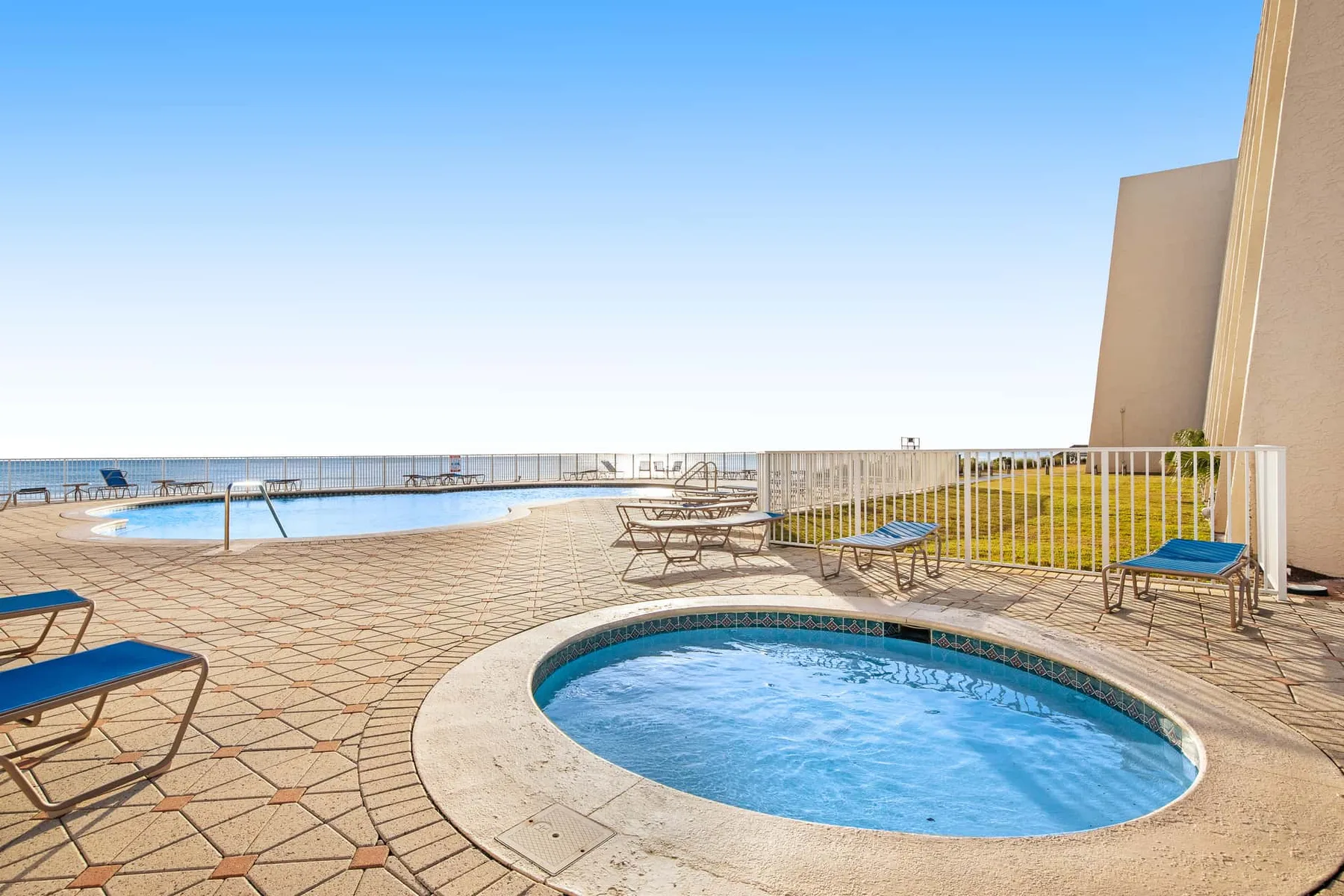 An outdoor pool area with a tiled deck and lounge seating overlooks the sea.