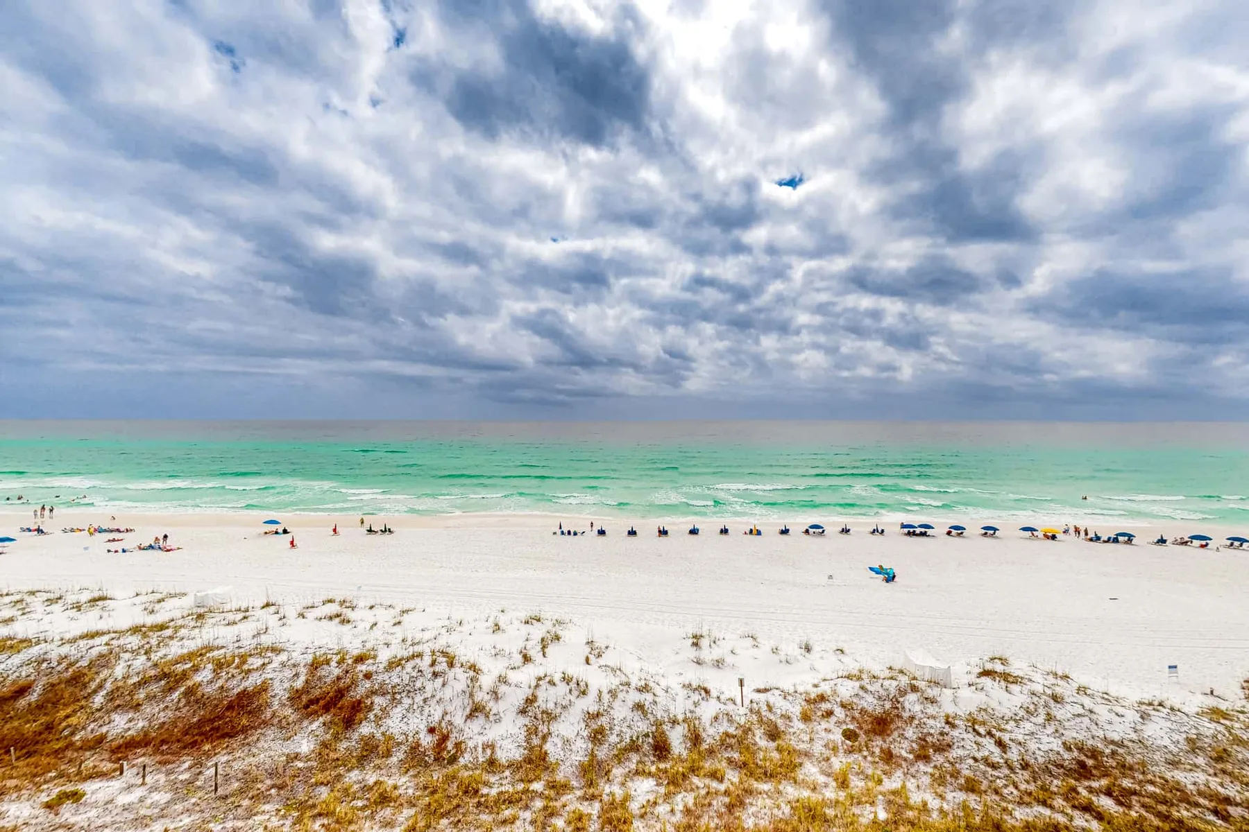 A sandy beach meets turquoise water beneath a cloudy sky.