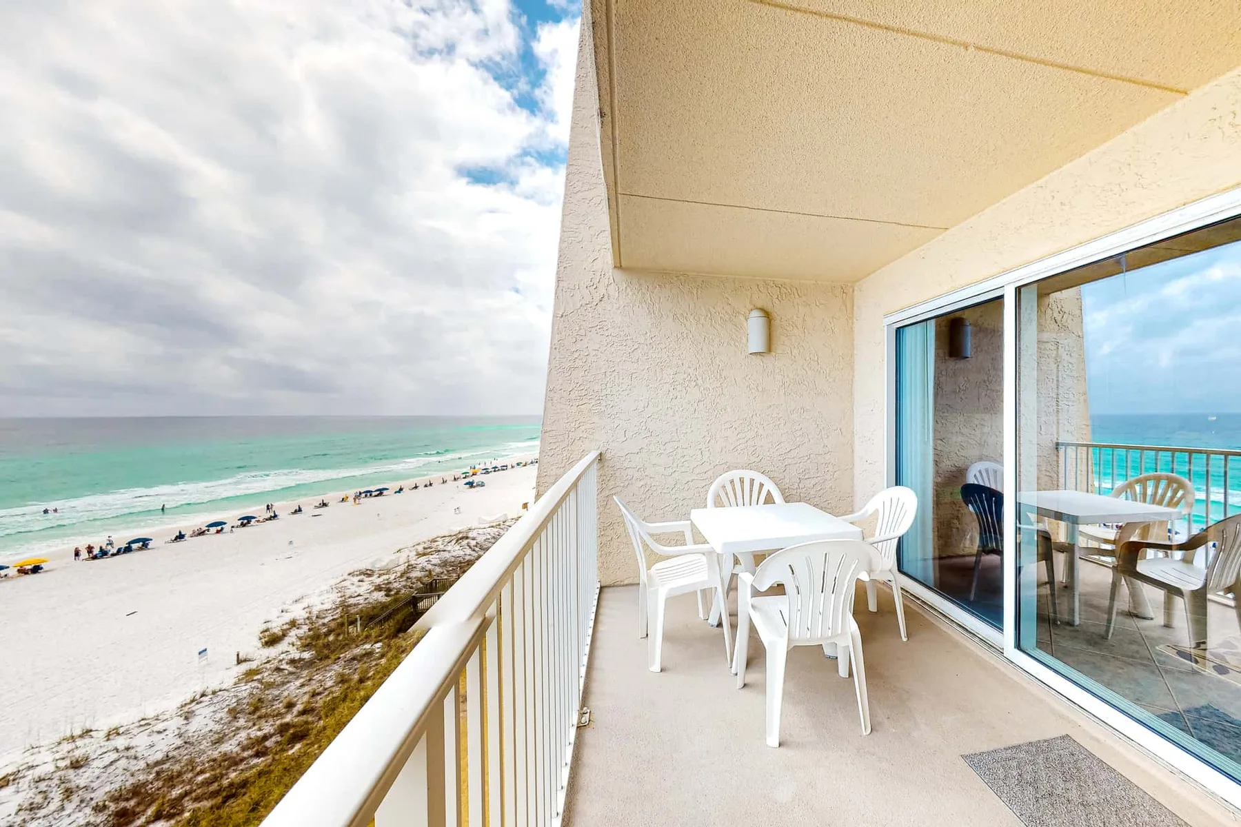 A balcony dining area overlooks a sandy beach and the ocean.