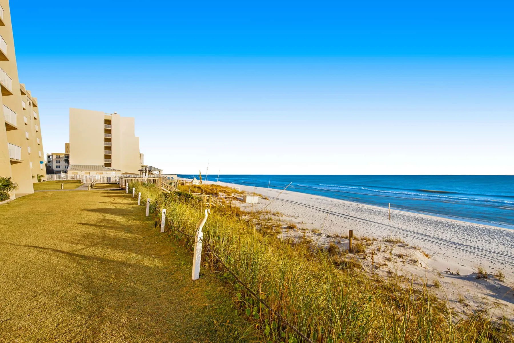 A beachfront scene with buildings beside a sandy shore and blue ocean.
