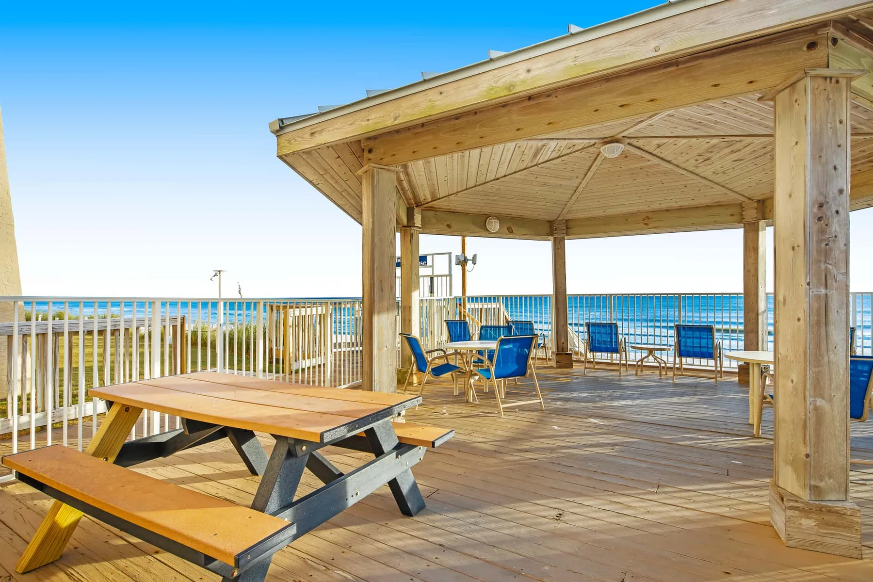 A wooden deck with a covered seating area and picnic table overlooks the ocean.