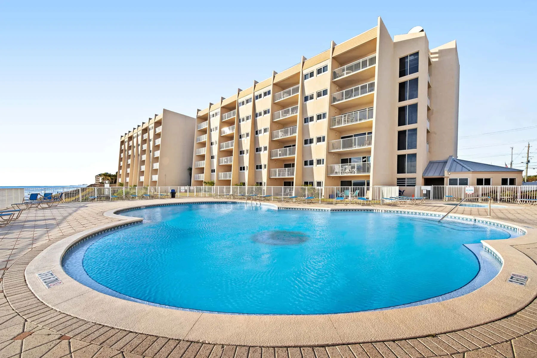 A swimming pool sits in front of a multi-story building under a clear sky.