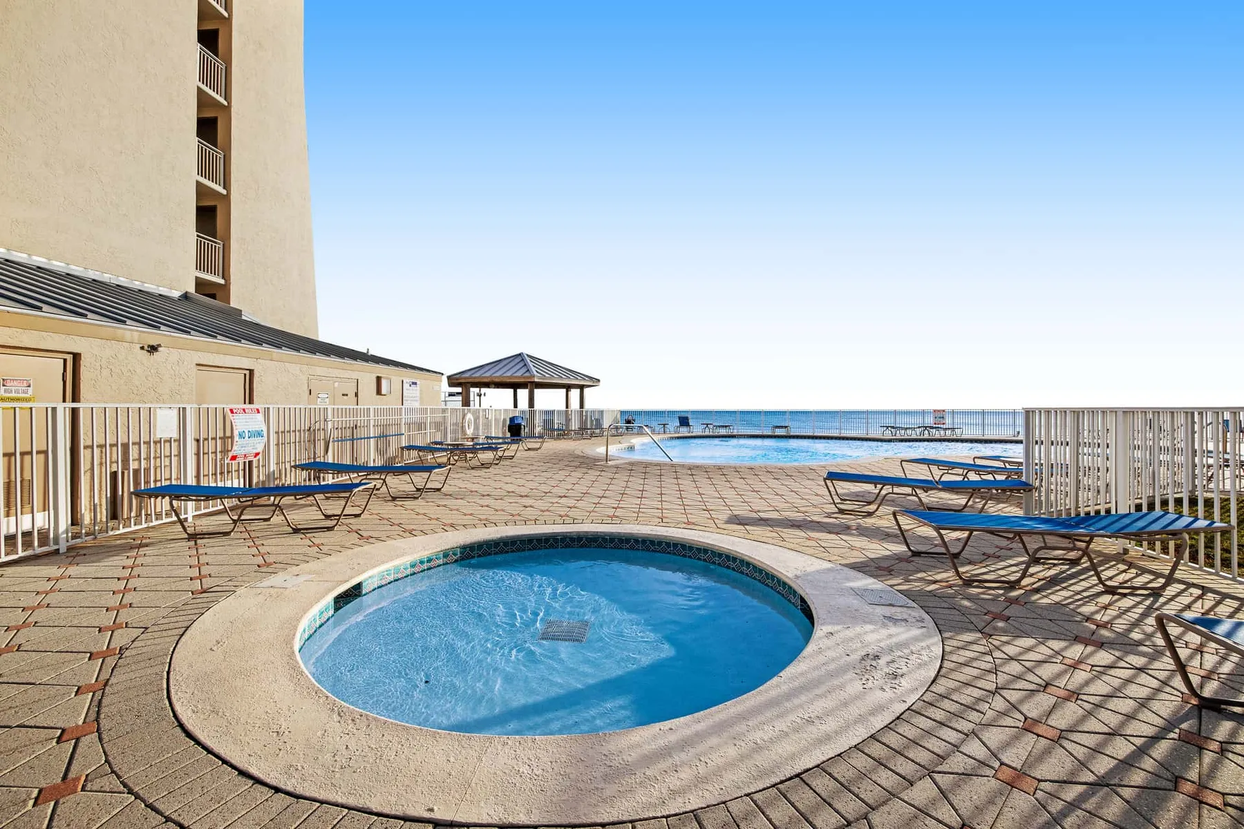 An outdoor pool is surrounded by a tiled deck with lounge chairs and ocean views.