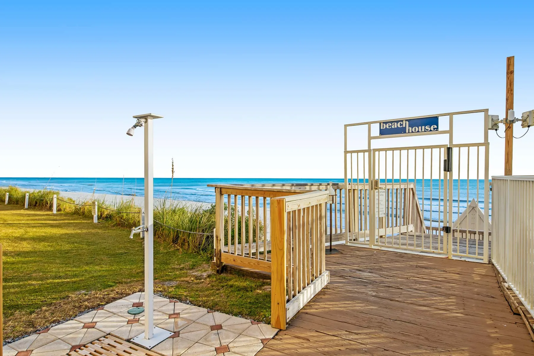 A wooden deck and railing overlook the ocean beside a grassy area.