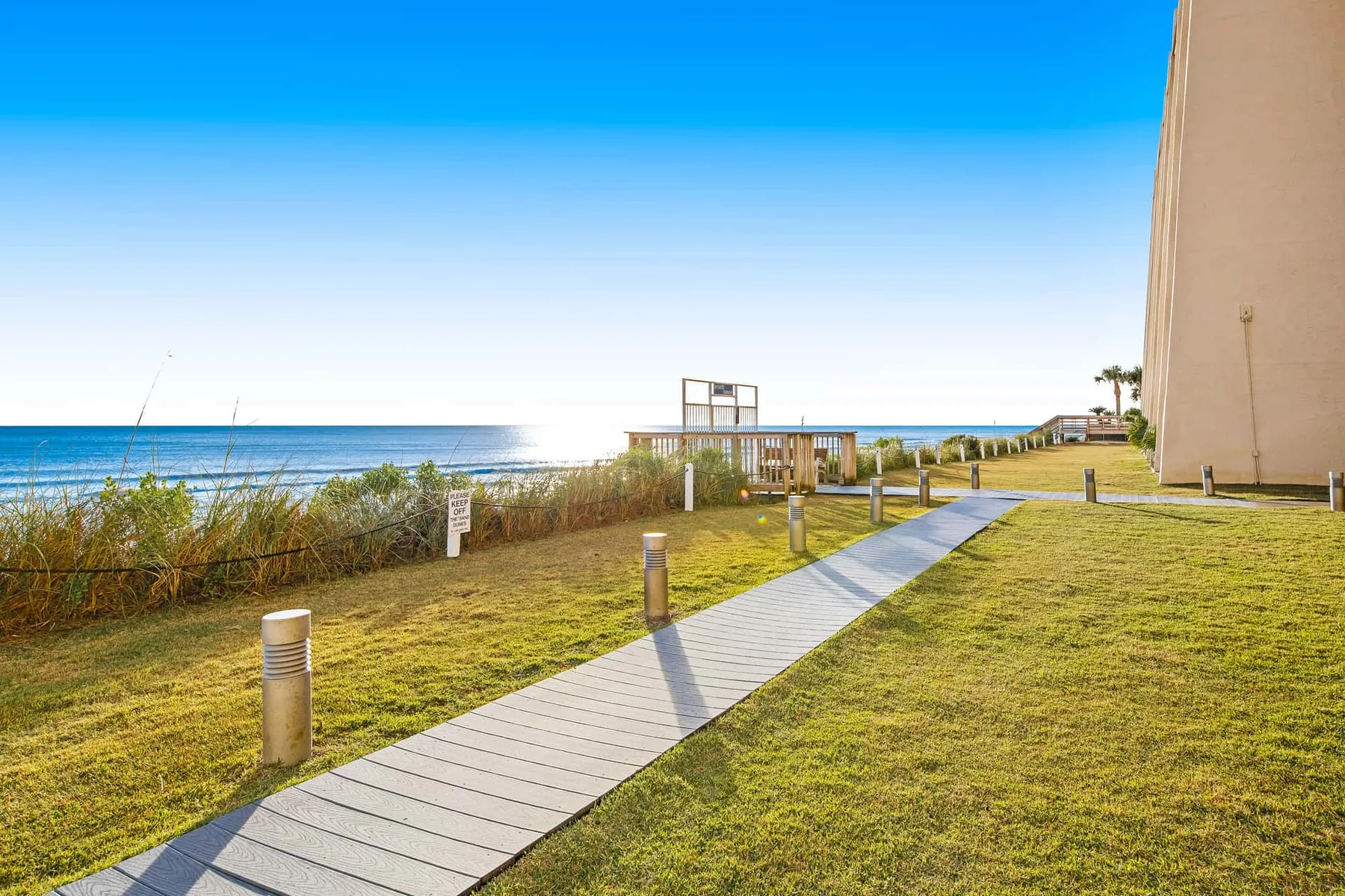A paved walkway crosses a grassy seaside area beside the ocean.