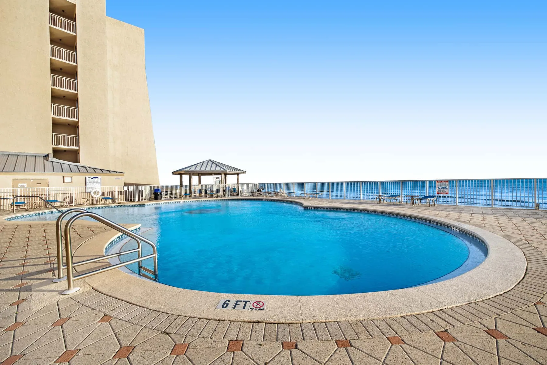 A swimming pool beside a tall building, with the ocean visible beyond.