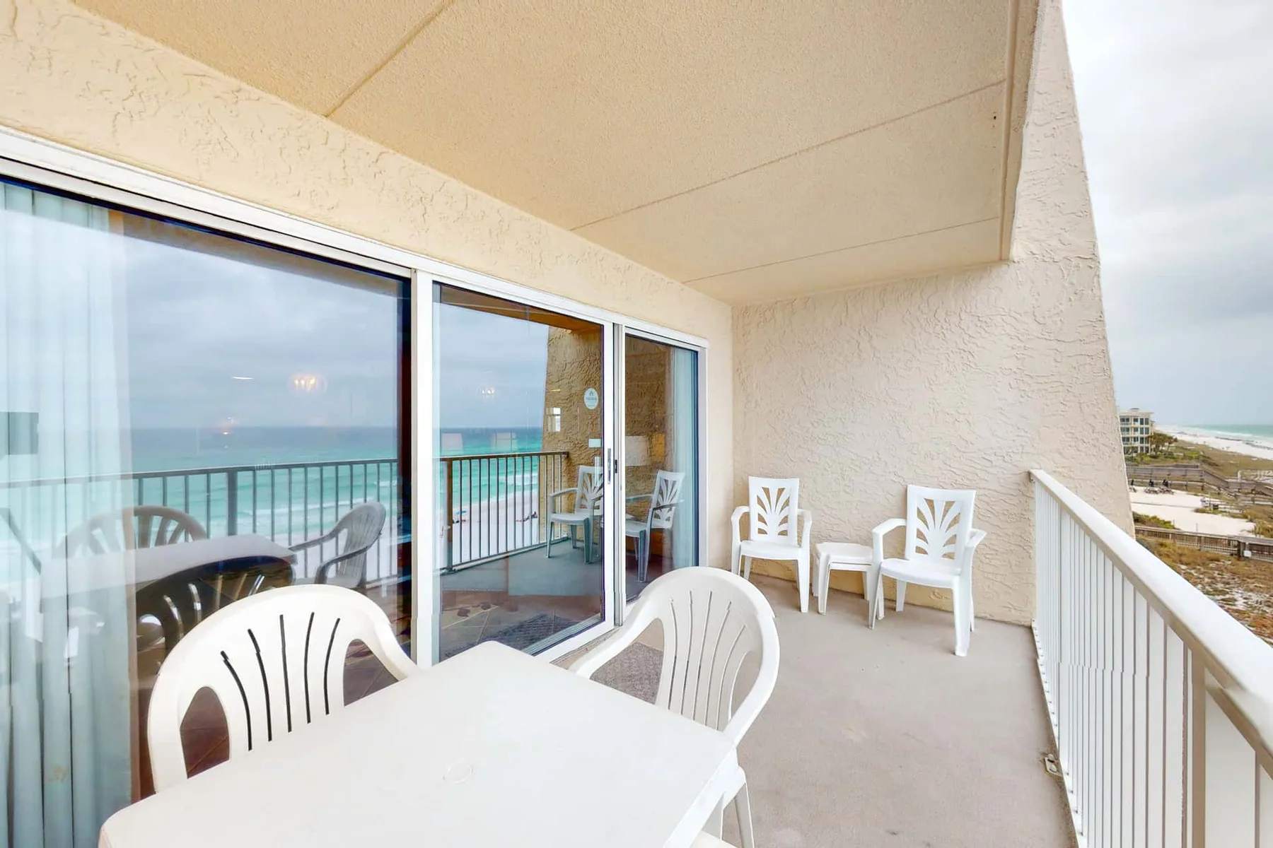 A covered balcony has a white table and chairs beside sliding glass doors.
